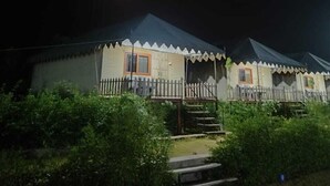 En række små hytter i et plan med veranda, omgivet af grøn bevoksning, og med et hvidt stakhegn.