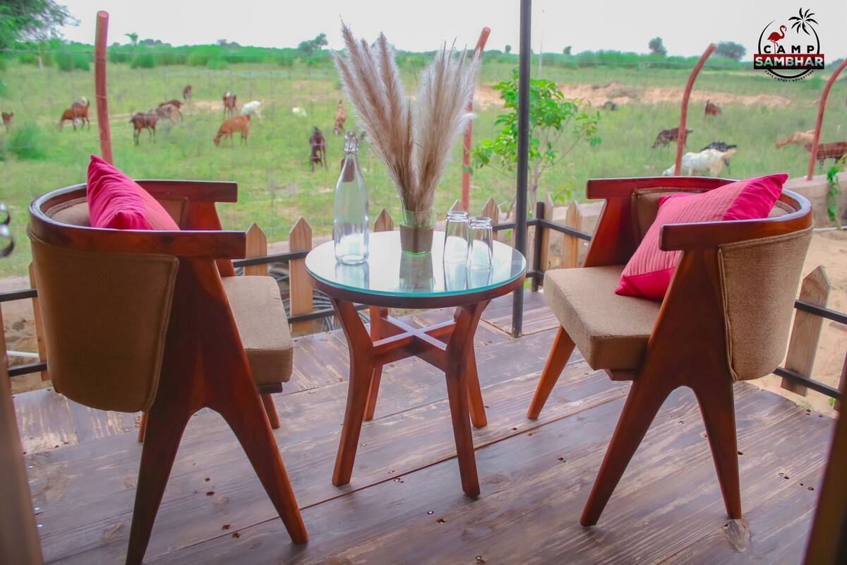 A wooden deck with two chairs and a glass table, overlooking a field with grazing animals.