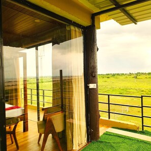 Una habitación con vistas a un campo verde, una mesa de madera, una silla y una ventana con cortinas.