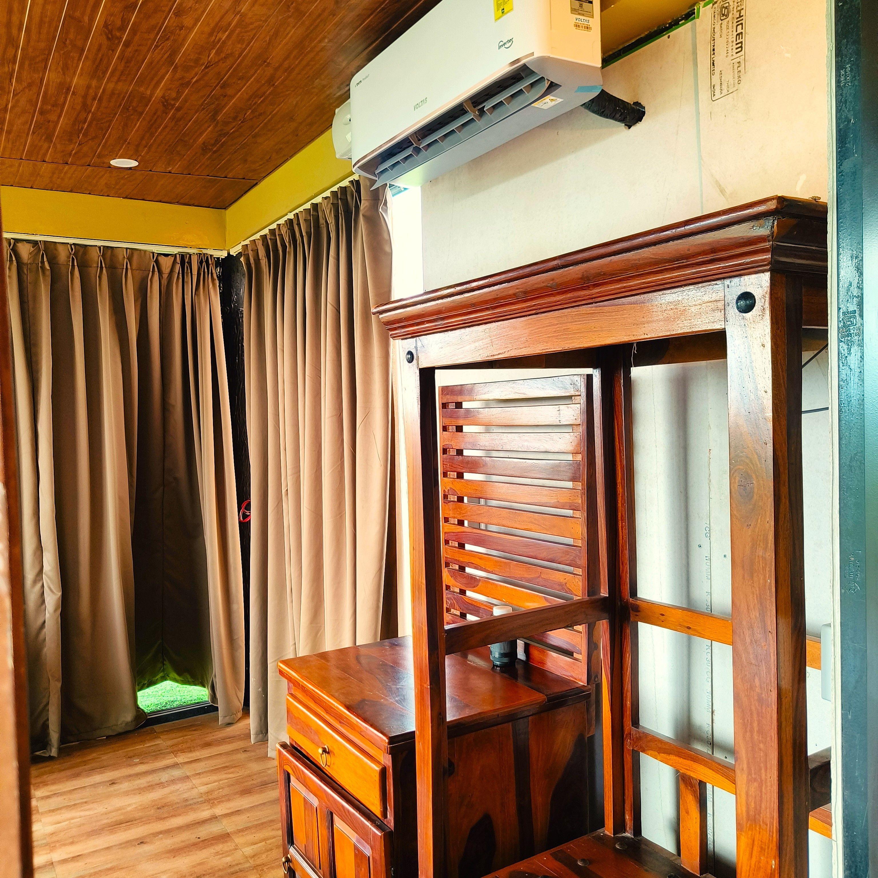 A room with a wooden ceiling, a ceiling fan, an air conditioning unit, a wooden cabinet, and a curtain.