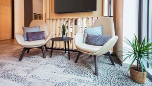 A modern room with two chairs, a small table, a potted plant, and a flat-screen TV mounted on a wooden panel. - B&B HOTEL Erfurt City-West (Erfurt)