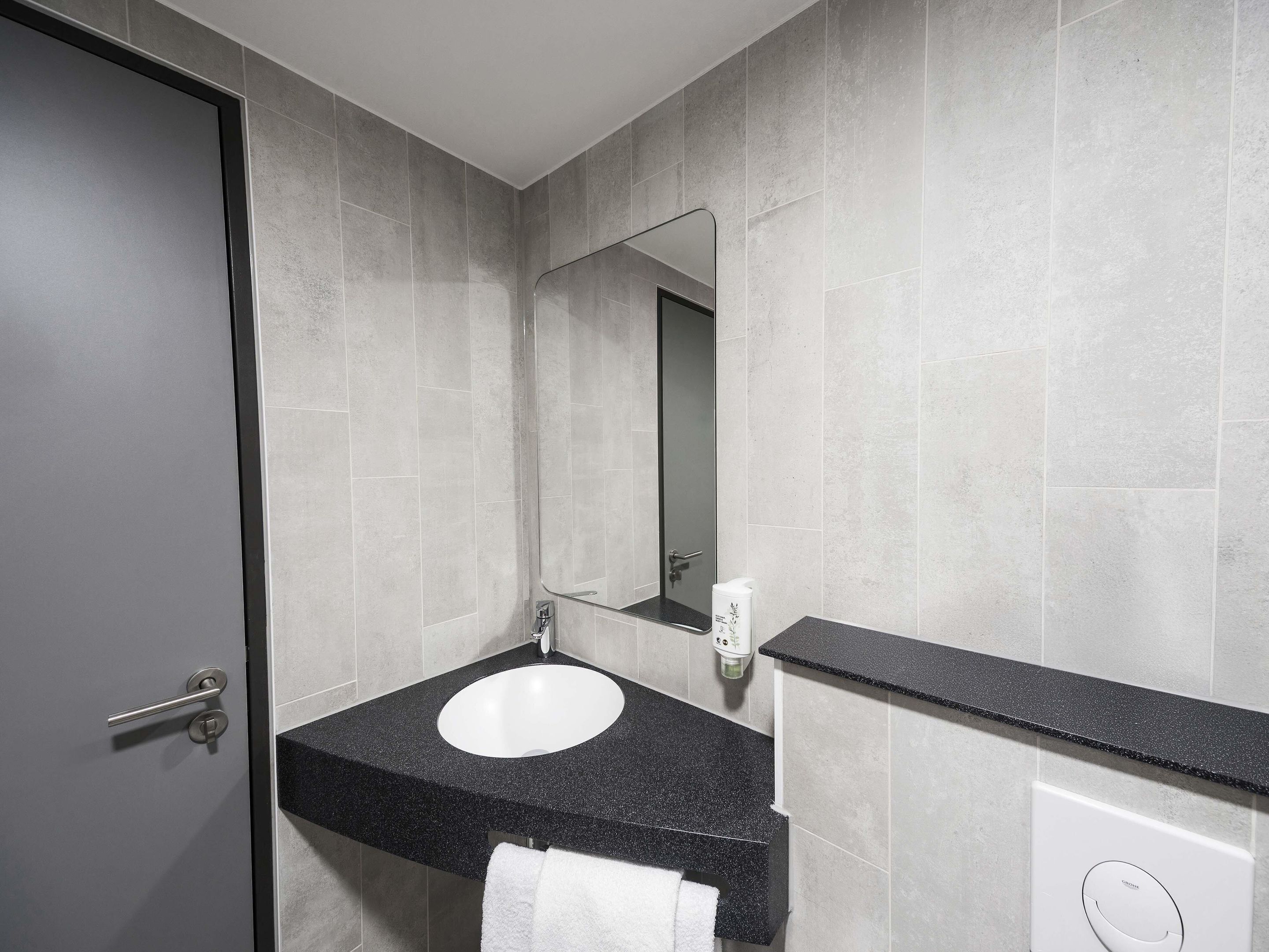A modern bathroom with a white sink, black countertop, and a large mirror.