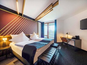 A modern hotel room with a bed, desk, and seating area.