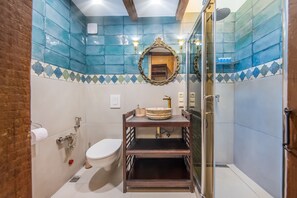A bathroom with a toilet, a sink with a decorative basin, a mirror, and a shower area.