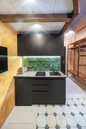 A compact kitchen with a black countertop, stainless steel appliances, and a green tiled backsplash.