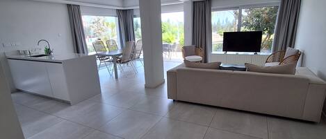 A spacious living area with a large sofa, a flat-screen TV, and a dining area with chairs.