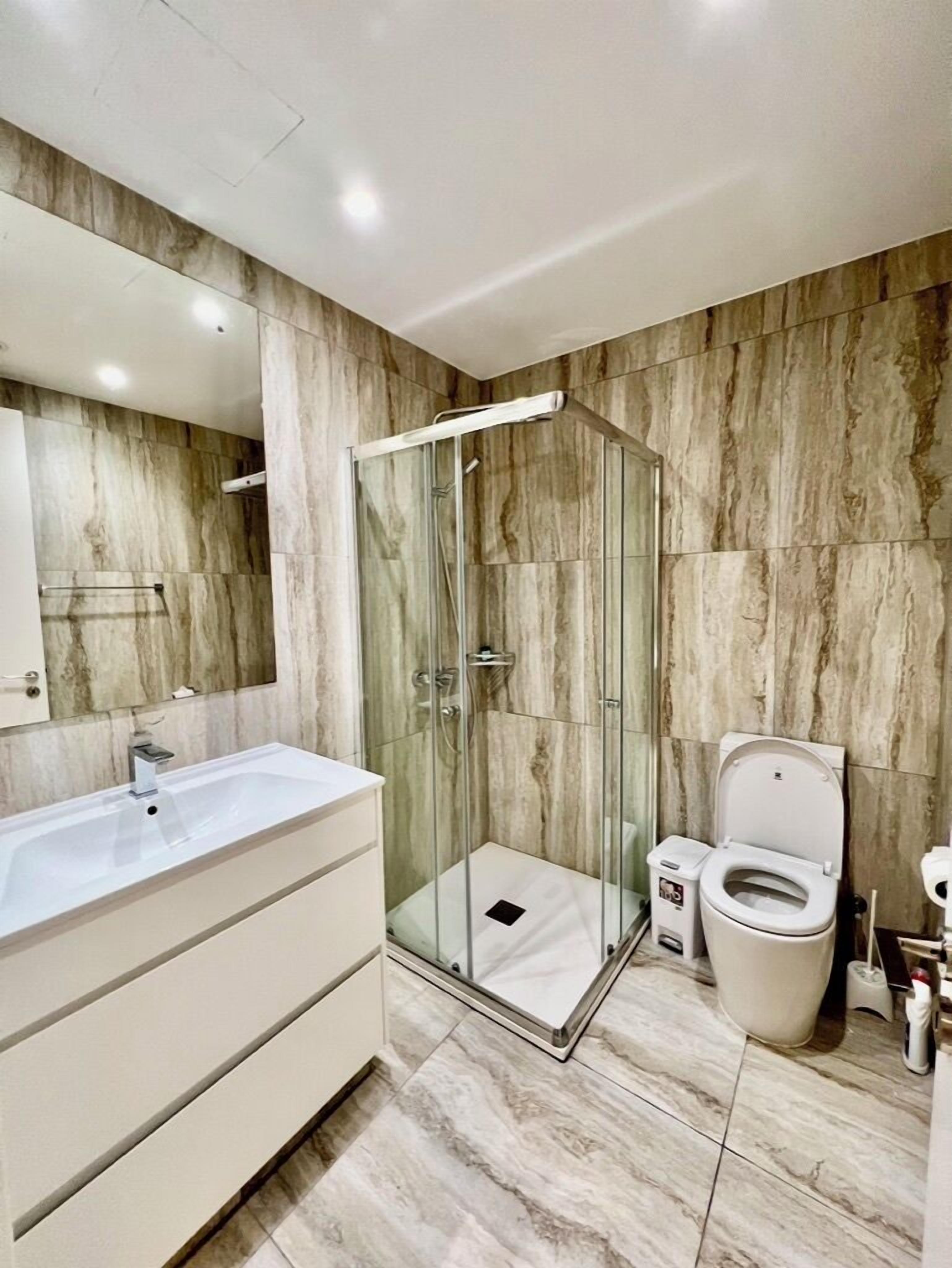 Un baño moderno con ducha de vidrio, lavamanos blanco y retrete.