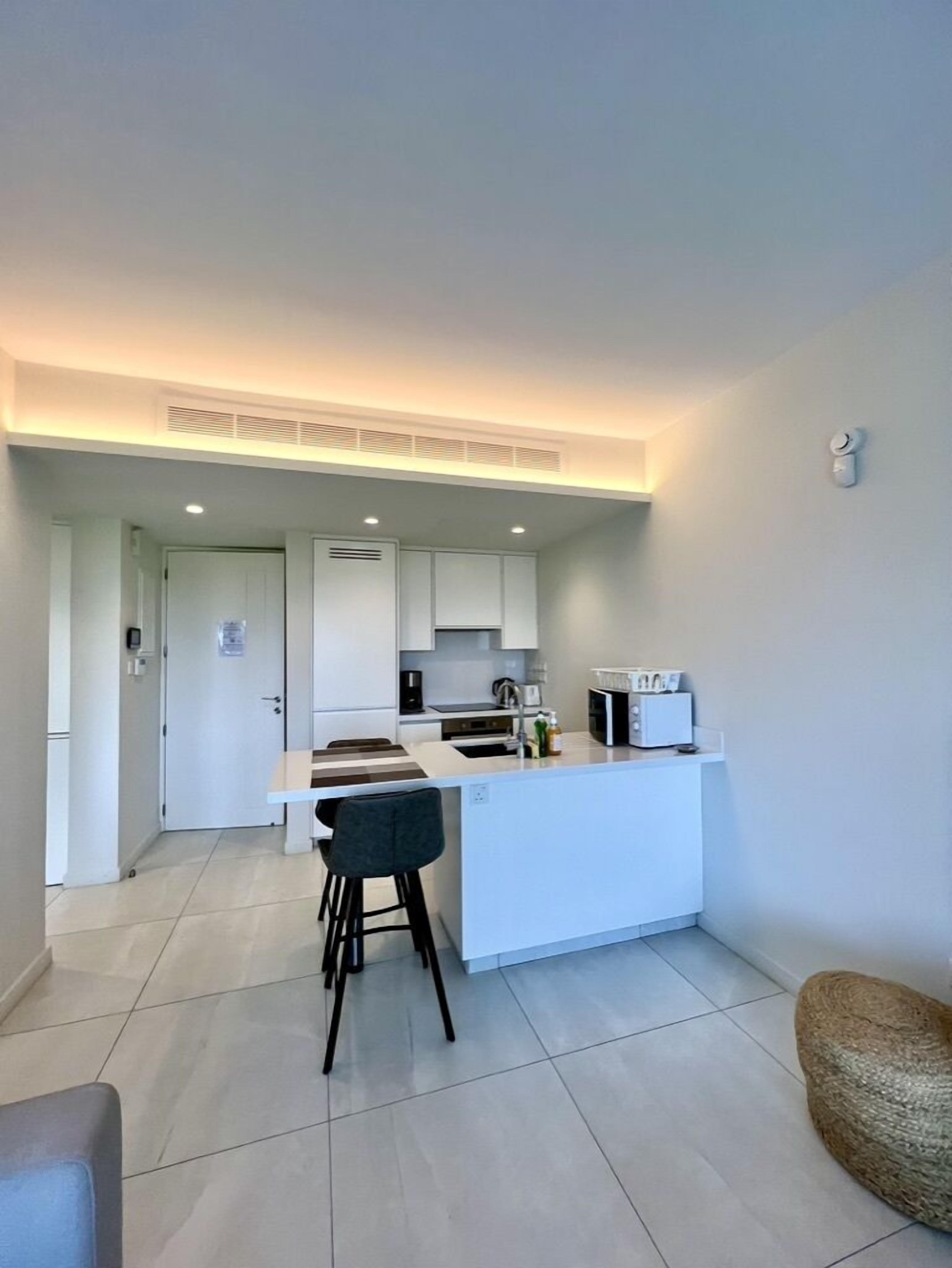 Una cocina funcional con armarios blancos, una isla central y un taburete de bar.