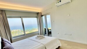 A modern bedroom with a large bed, a view of the ocean, and a ceiling fan. - Emerald Bay Suites (Paralimni)