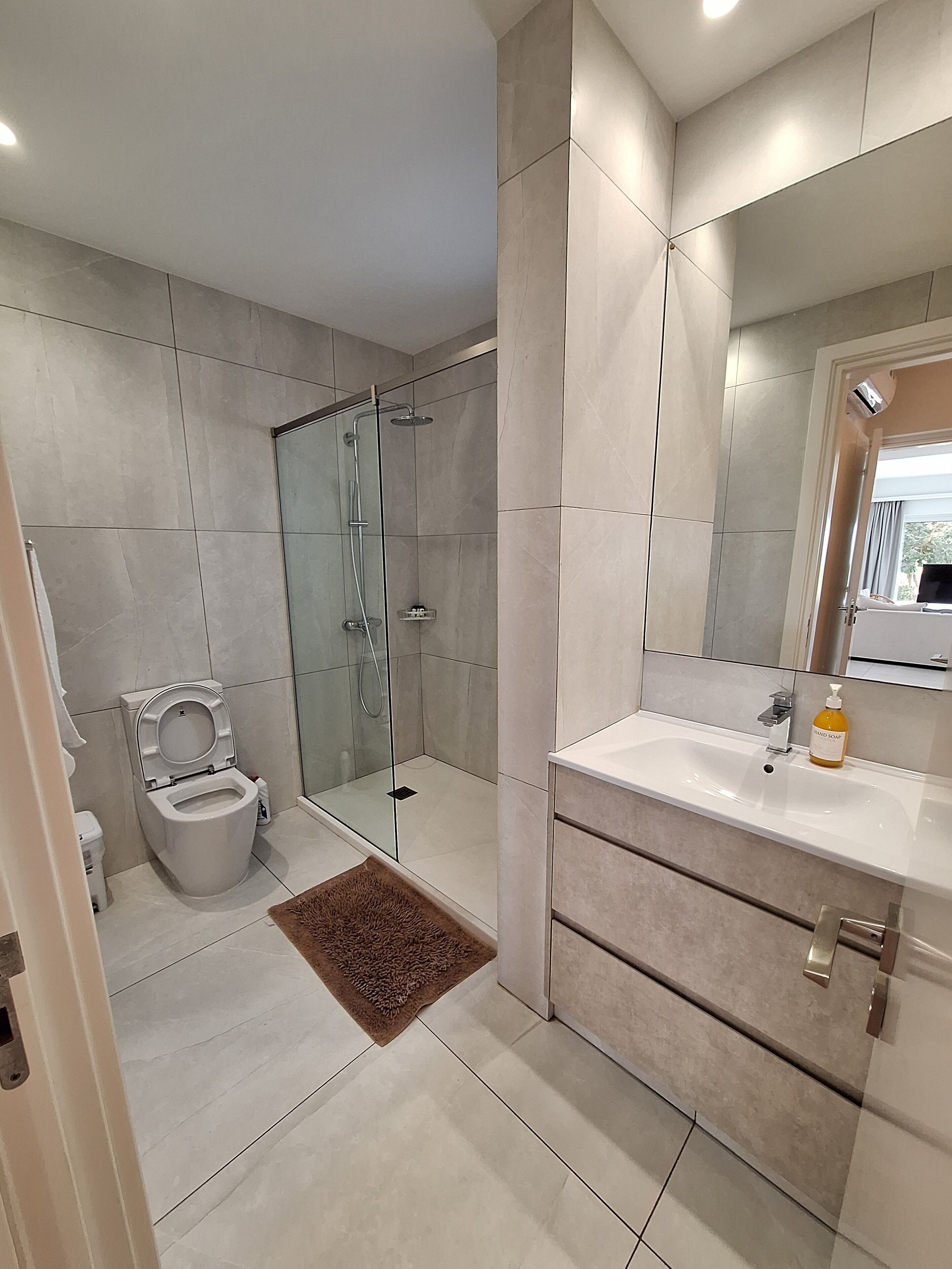 A modern bathroom with a glass-enclosed shower, a toilet, and a vanity with a mirror.