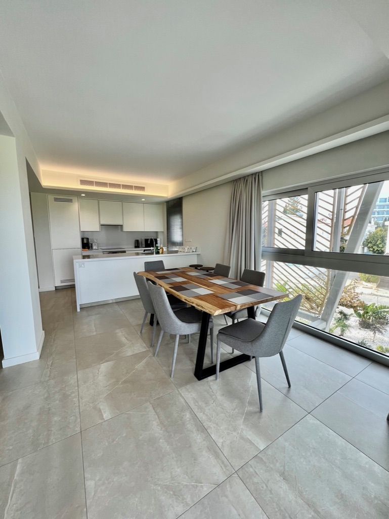 Une cuisine moderne avec des meubles blancs, un îlot central et un coin repas comprenant une table et des chaises en bois.