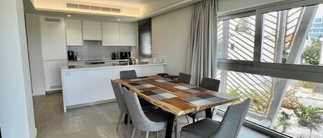 Une cuisine moderne avec des meubles blancs, un îlot central et un coin repas comprenant une table et des chaises en bois.