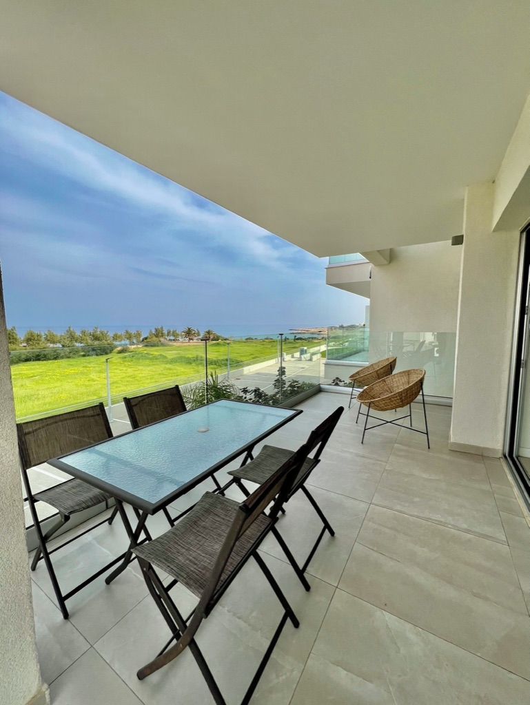 Un balcón con mesa y sillas de vidrio, con vistas a un paisaje verde y al mar.