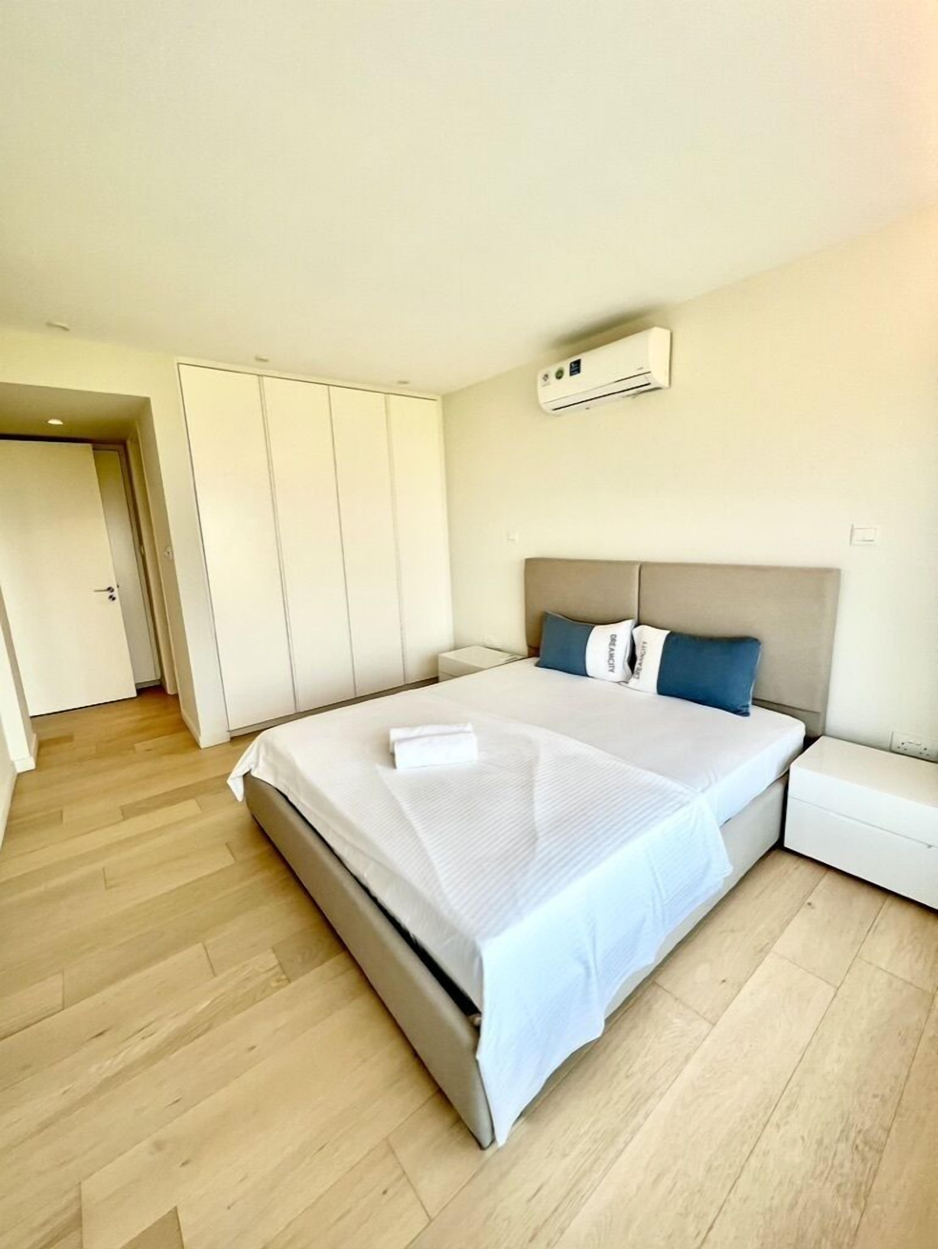 A modern bedroom with a large bed, white bedding, a grey headboard, and a white nightstand.