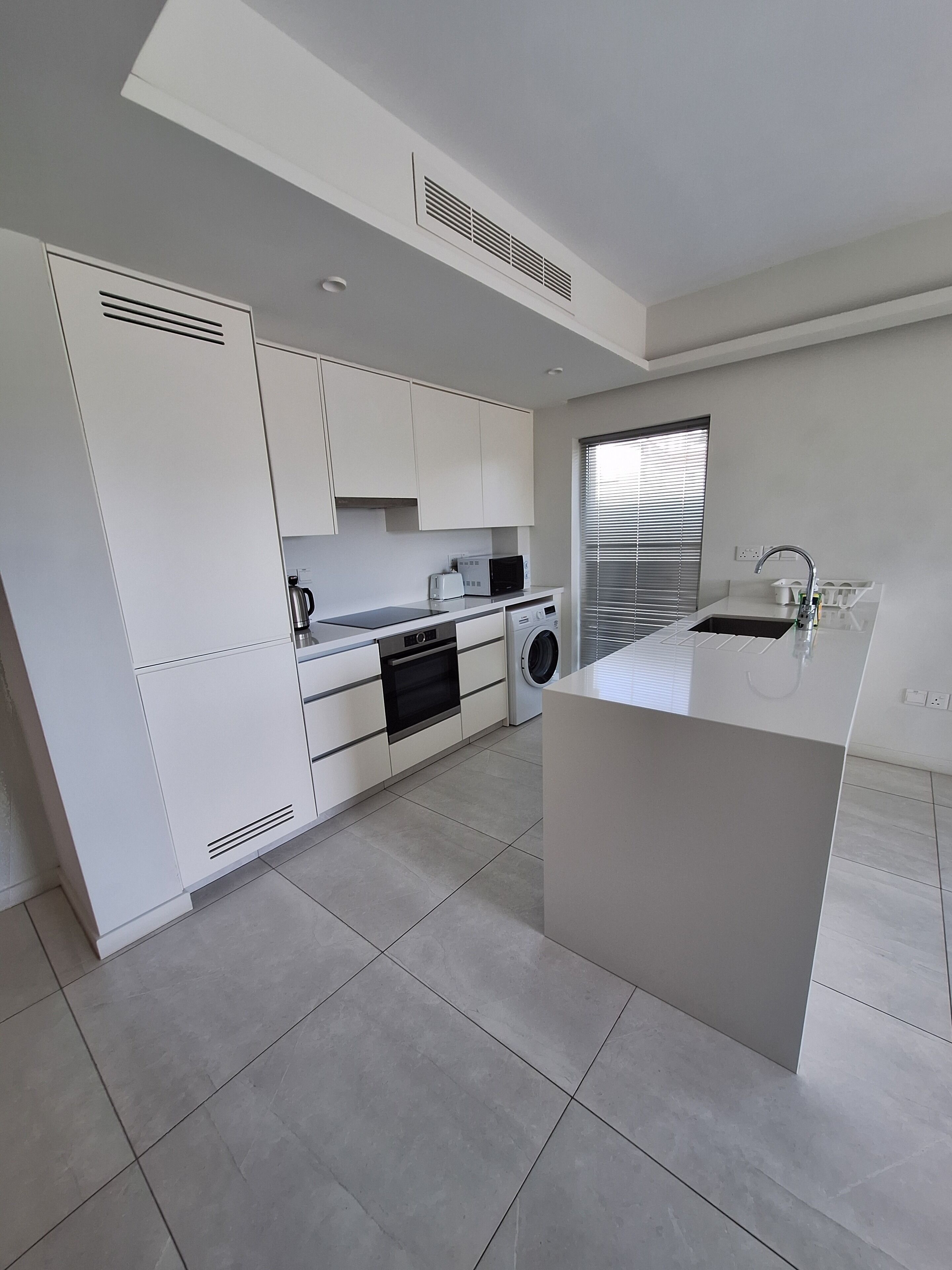 A modern kitchen with white cabinetry, a built-in oven, a microwave, and a sink.