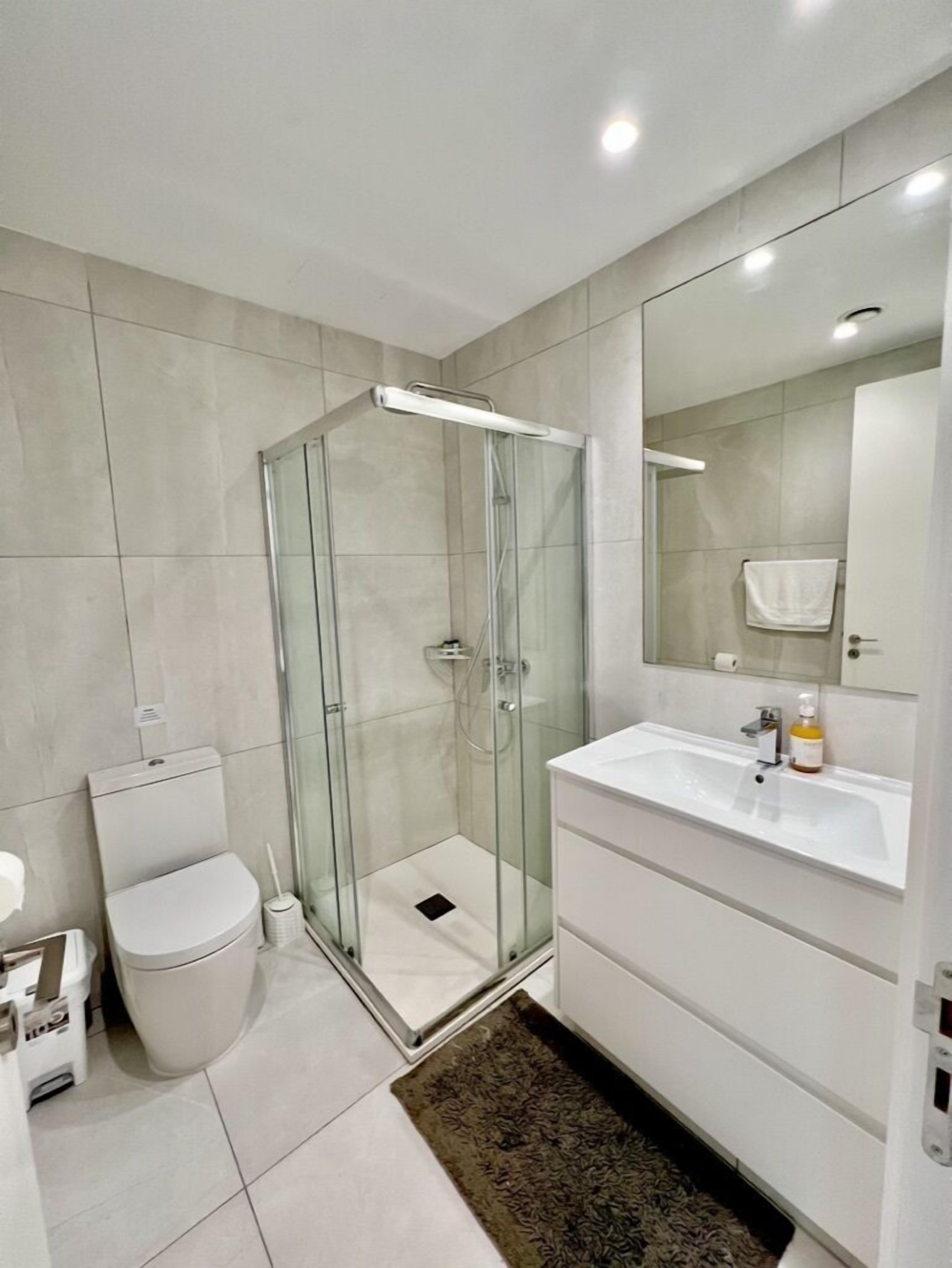 A modern bathroom with a glass-enclosed shower, a white toilet, and a vanity with a mirror.