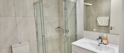 A modern bathroom with a glass-enclosed shower, a white toilet, and a vanity with a mirror.