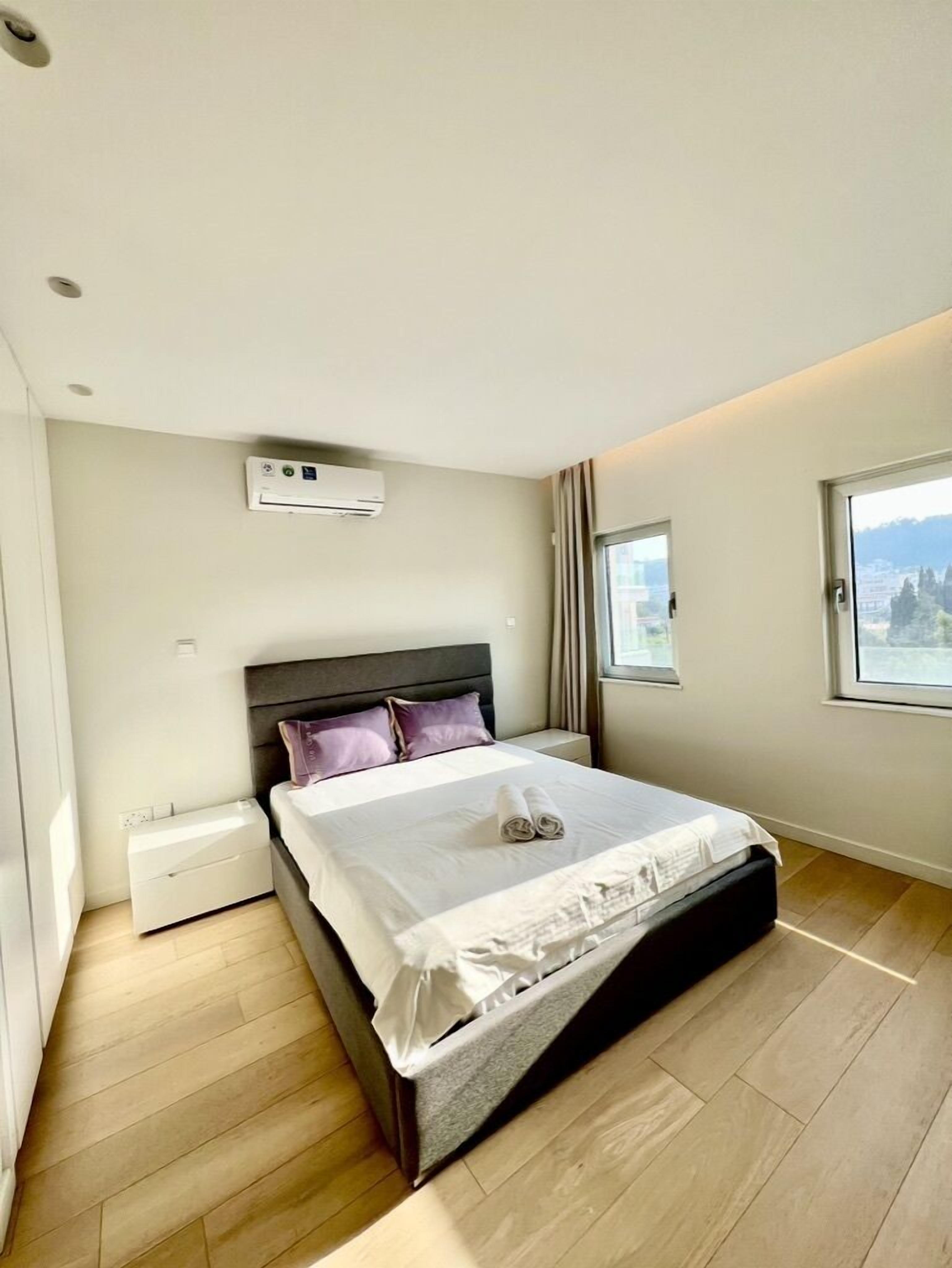 Een moderne slaapkamer met een bed, nachtkastje, raam en uitzicht op het groen.