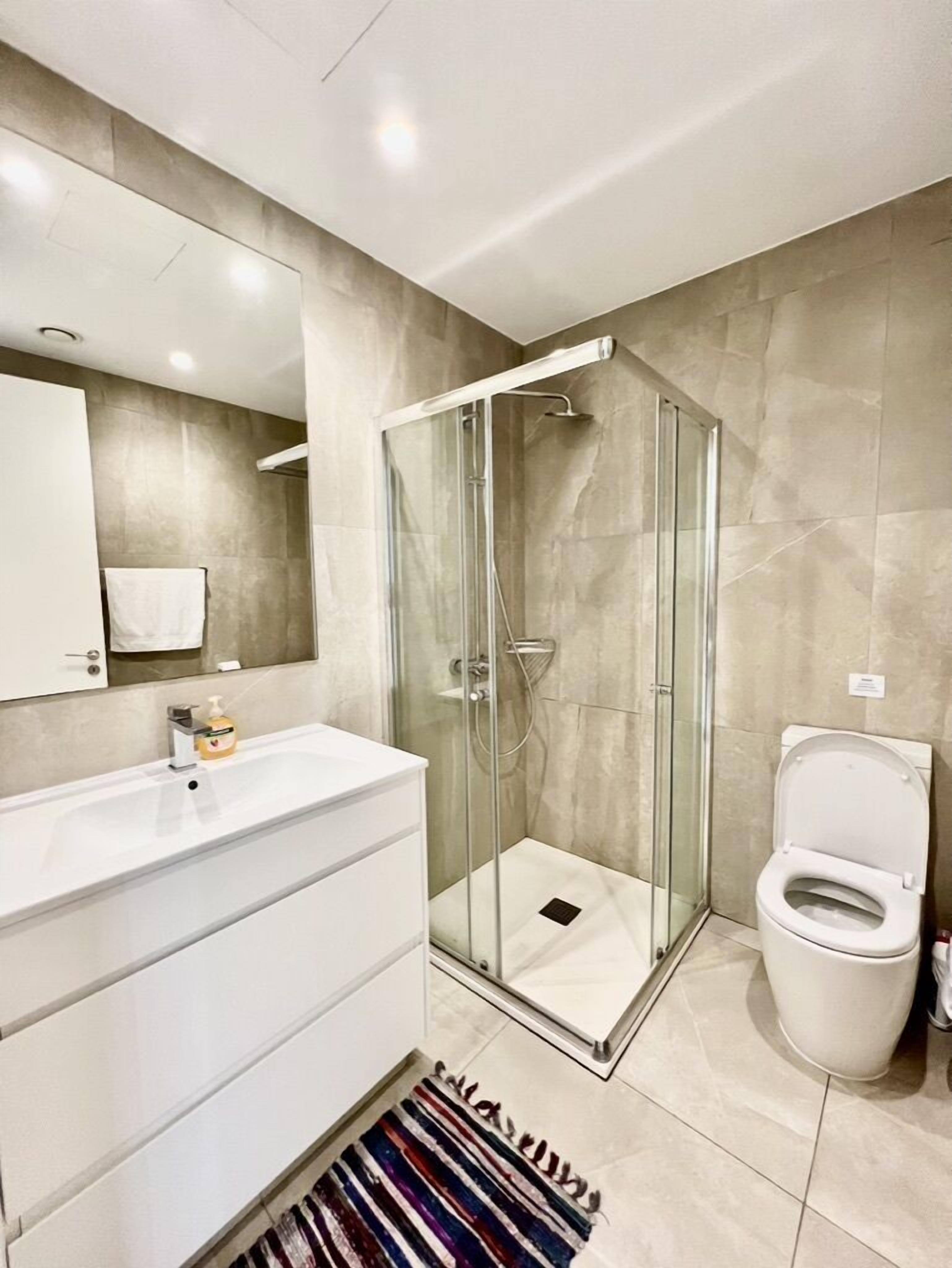A modern bathroom with a glass-enclosed shower, a white sink, and a toilet.