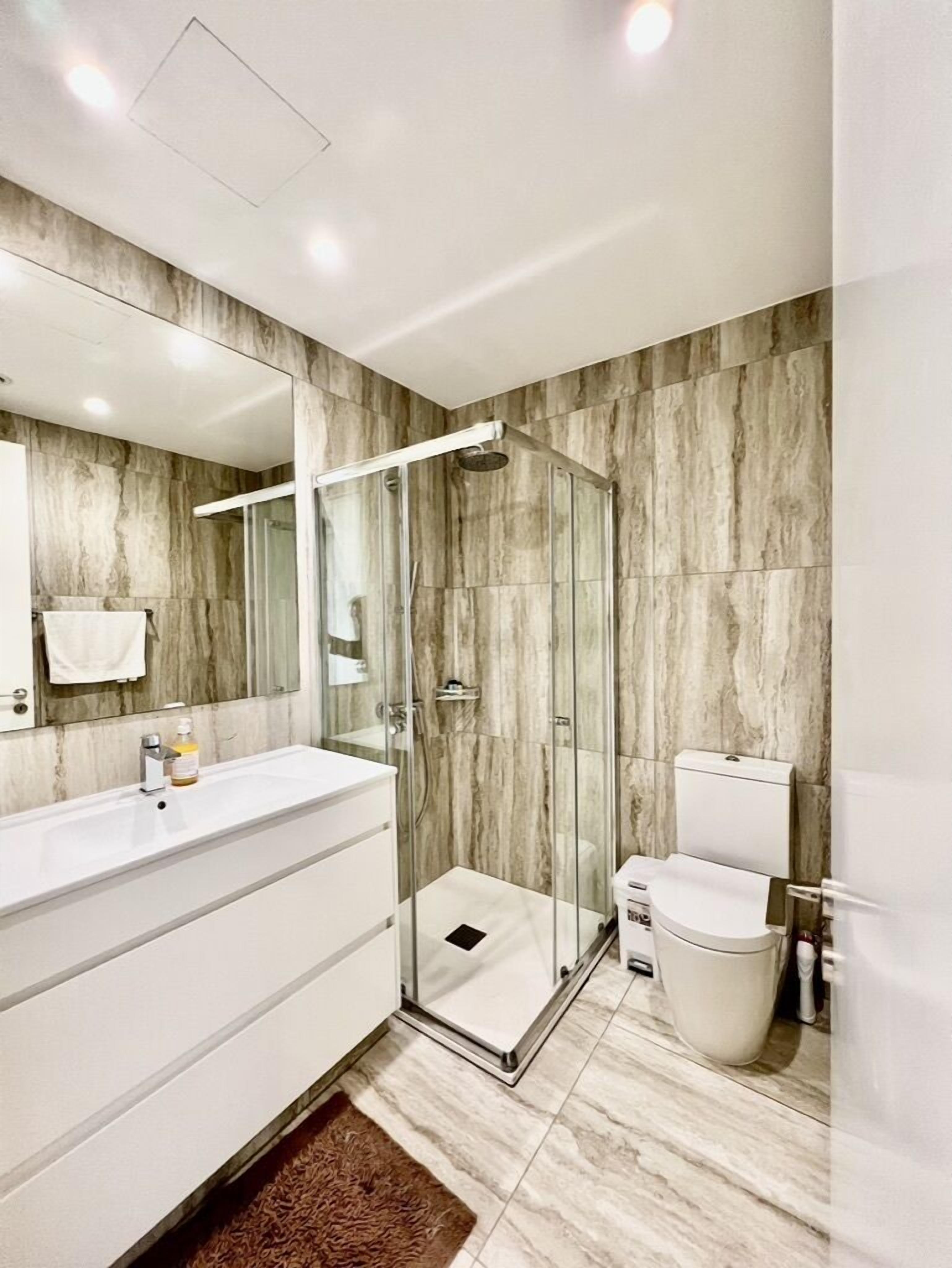 A modern bathroom with a glass-enclosed shower, a white vanity, and a marble backsplash.