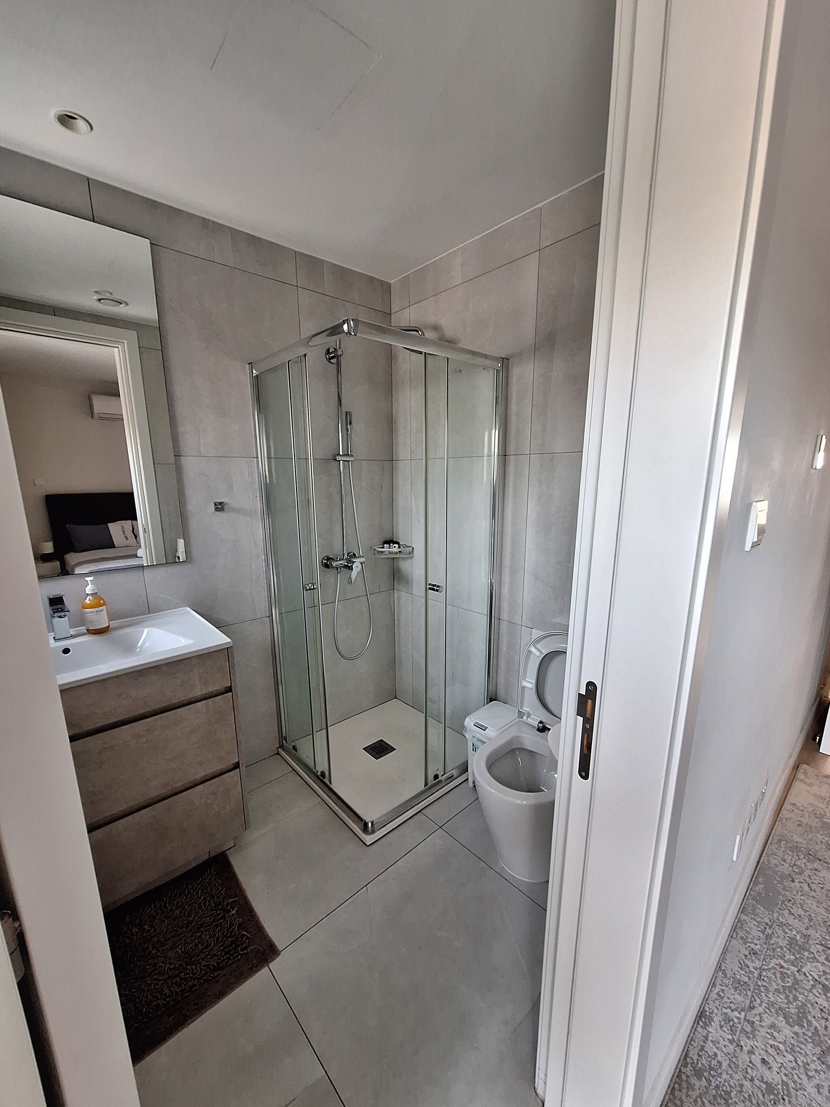 Een moderne badkamer met een douchecabine van glas, een wit wastafeltje en een toilet.