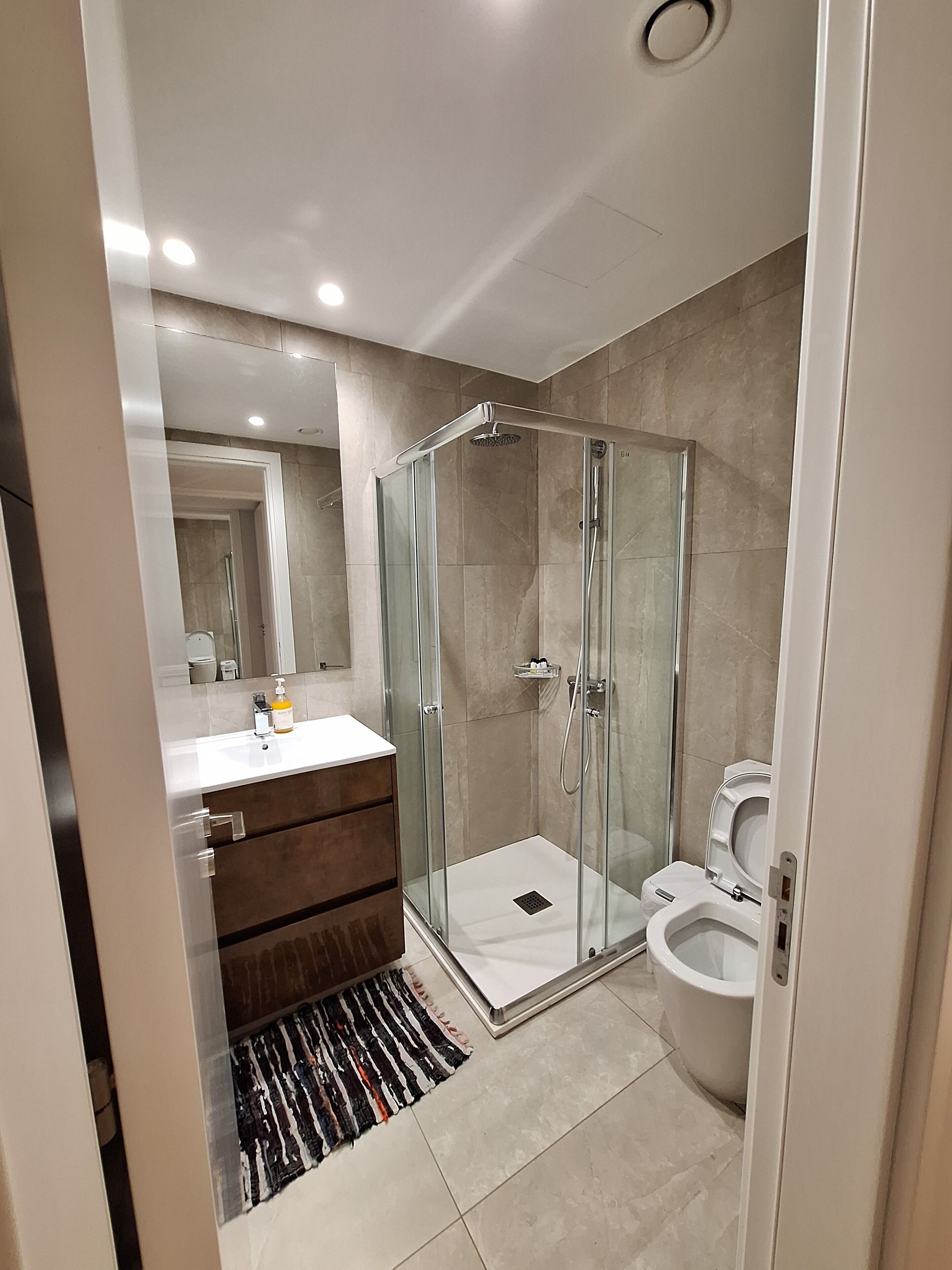 Une salle de bain moderne avec une douche à parois de verre, des toilettes blanches et un meuble-lavabo avec un miroir.