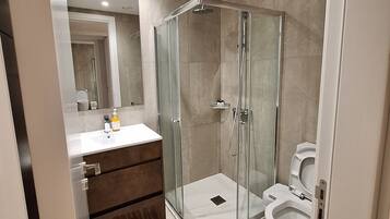 Une salle de bain moderne avec une douche à parois de verre, des toilettes blanches et un meuble-lavabo avec un miroir.