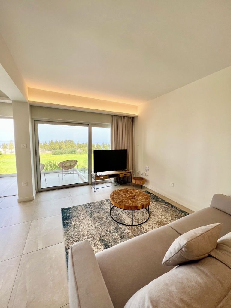 A modern living room with a sofa, a round coffee table, a flat-screen TV, and a sliding glass door leading to an outdoor area.