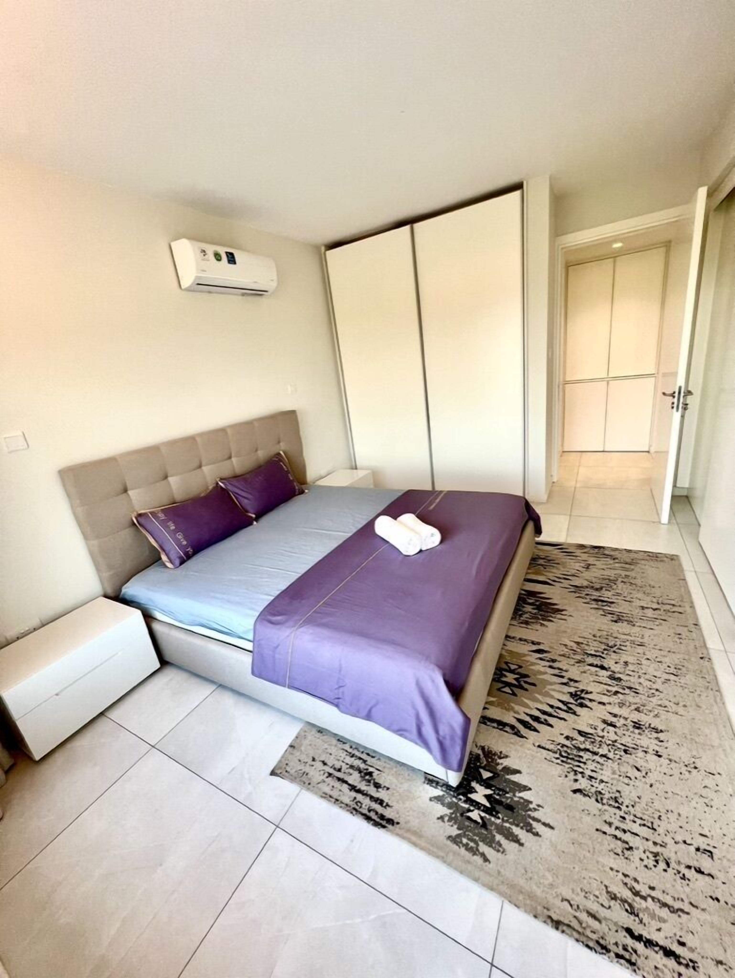 A bedroom with a bed, a nightstand, a wall-mounted air conditioner, and a sliding door closet.