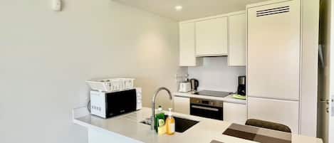 A compact kitchen with a white countertop, a built-in microwave, a sink, and a stove.