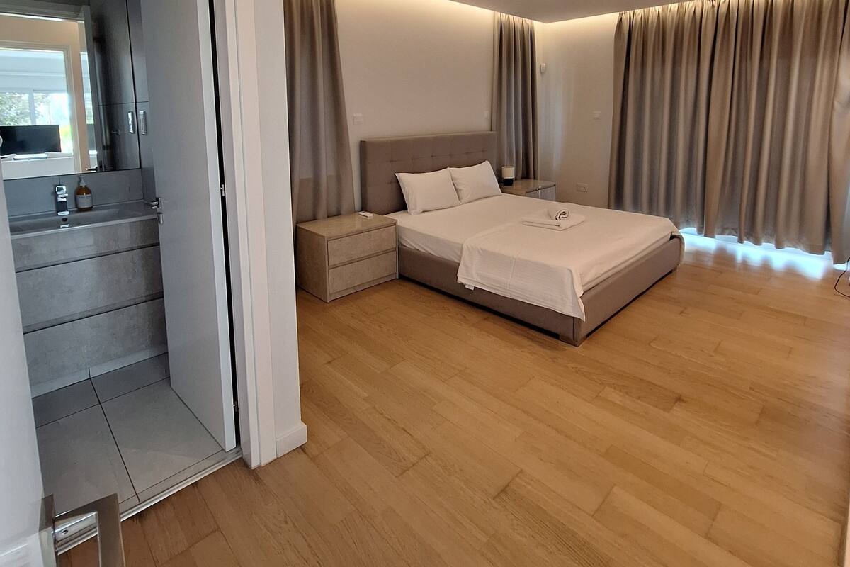 A modern bedroom with a large bed, a nightstand, a built-in wardrobe, and a bathroom visible through an open door.