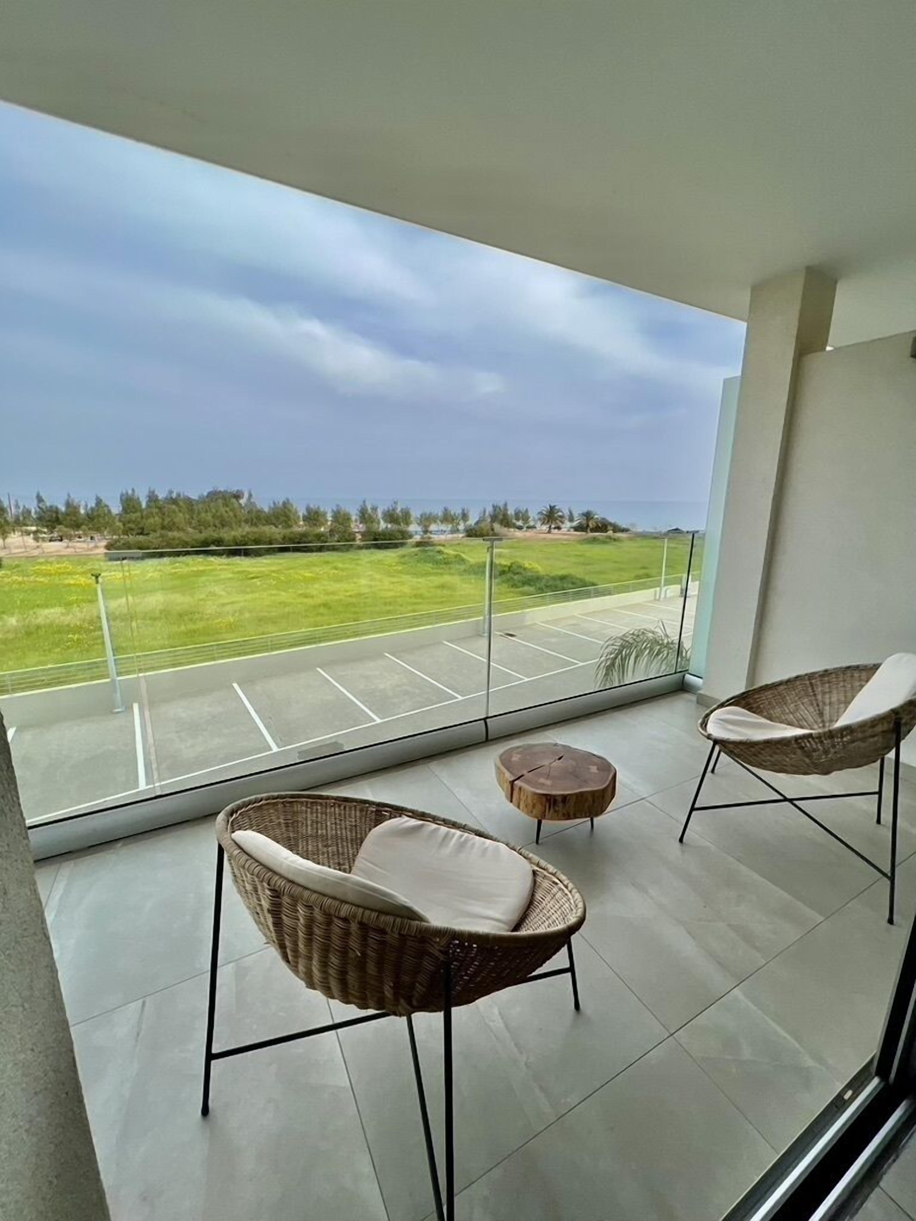 Un balcon avec deux fauteuils en osier et une petite table ronde, donnant sur un paysage verdoyant sous un ciel dégagé.