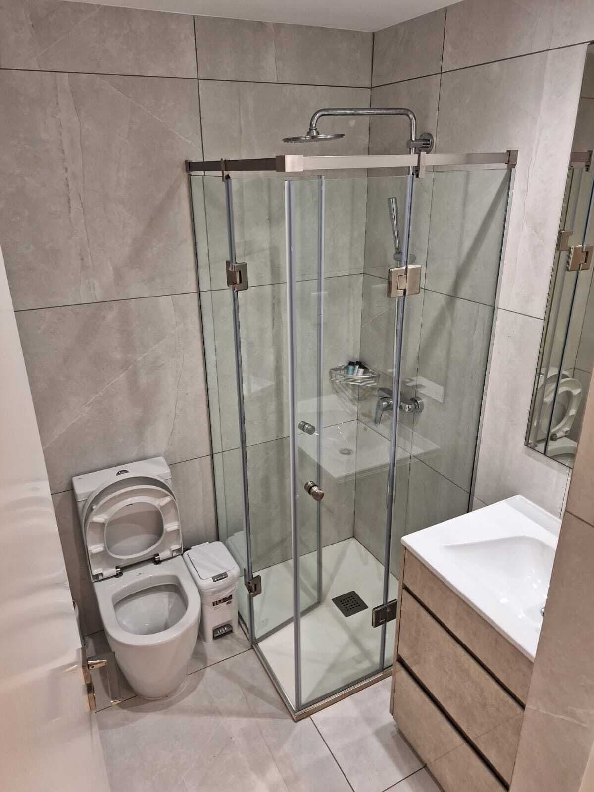 A modern bathroom with a glass-enclosed shower, a toilet, and a sink.