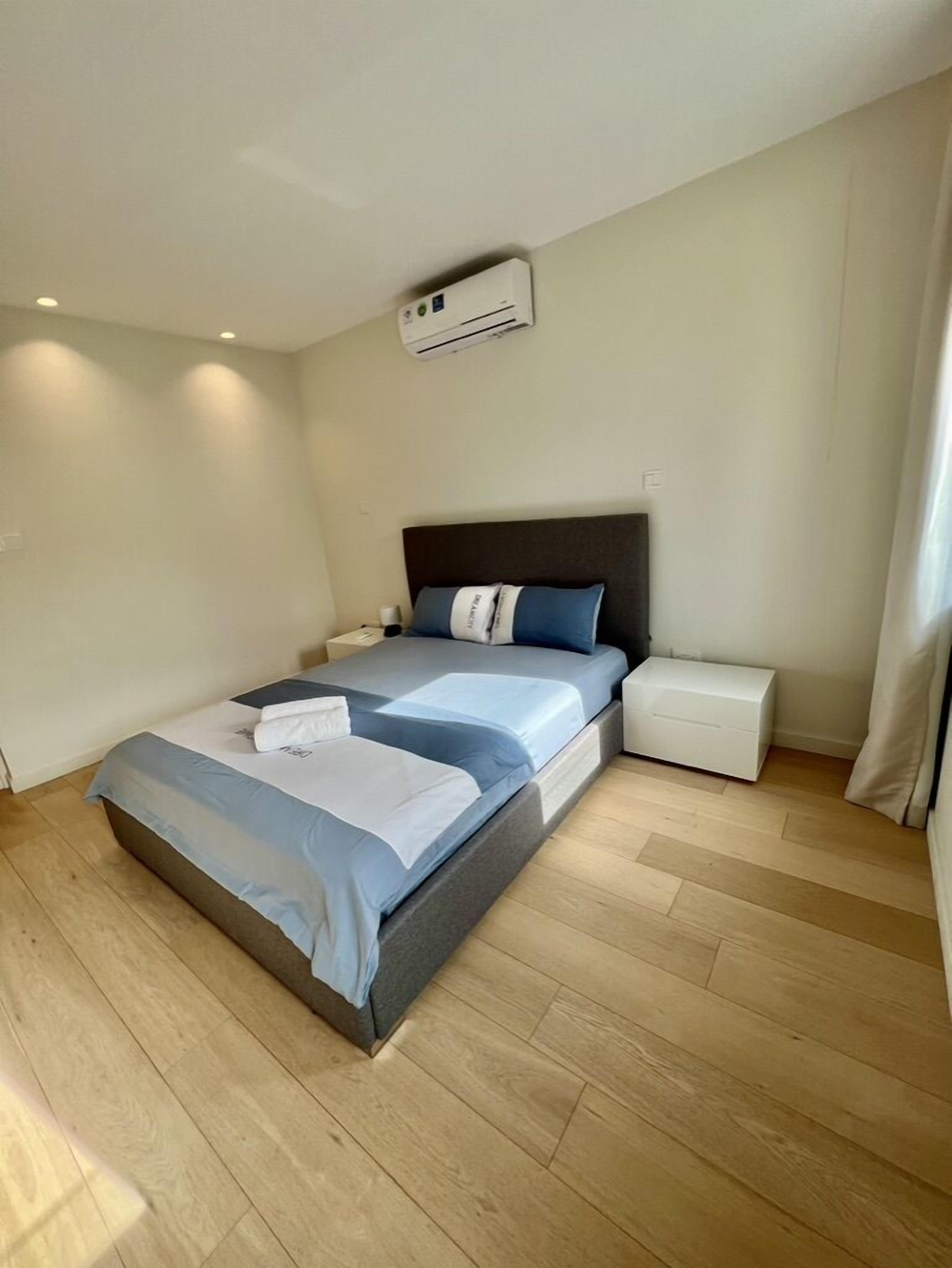 A modern bedroom with a single bed, a bedside table, a nightstand, an air conditioning unit, and a storage box.