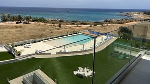 A pool area with a view of the sea, a sandy beach, and a grassy area with palm trees. - Emerald Bay Suites (Paralimni)