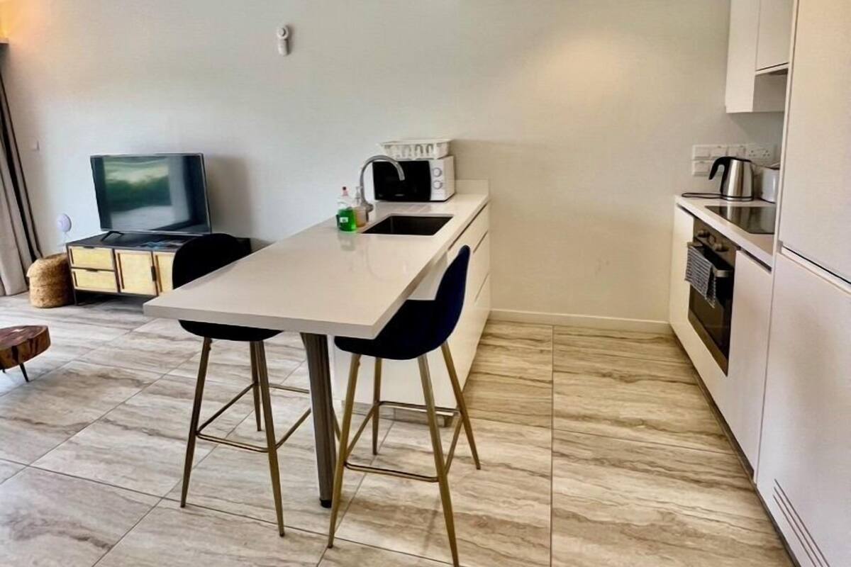 A modern kitchen with a dining area, white cabinetry, and a flat-screen TV.