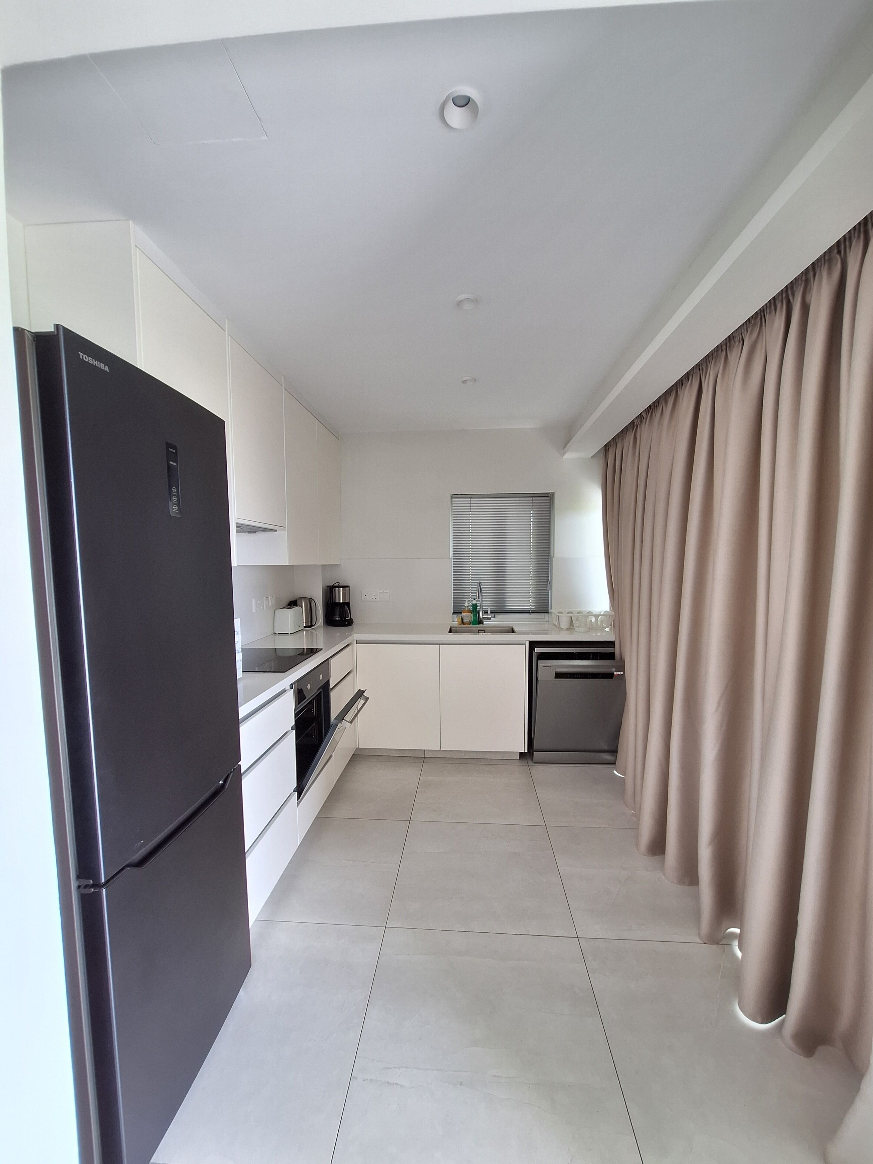 A modern kitchen with white cabinets, a black refrigerator, a built-in oven, and a dishwasher.