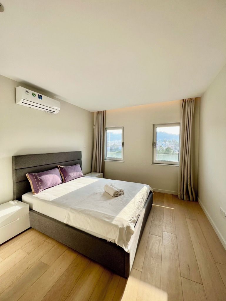 Un dormitorio moderno con una cama grande, un equipo de aire acondicionado y dos ventanas con cortinas.