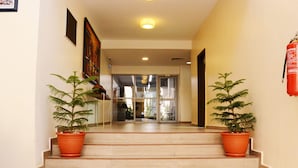 A hotel lobby with a staircase leading to a reception area. There are two potted plants on either side of the stairs. - GRACIAS HOTEL AND SUITES (Lekki)