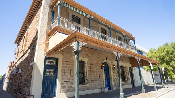 A two-story building with a balcony, a blue door, and a stone facade.
