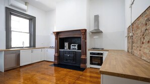 A kitchen with wooden flooring, white cabinets, a black stove, and a brick wall.