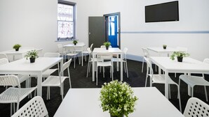 A conference room with white tables and chairs, a blue door, a TV on the wall, and potted plants.