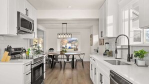 A modern kitchen with white cabinetry, stainless steel appliances, and a central island with chairs. - Newly Renovated Comfy Retreat (Spokane)