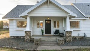 A single-story house with a gabled roof, a front porch with a bench, and a stone foundation. - Newly Renovated Comfy Retreat (Spokane)
