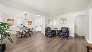 A spacious living area with a wooden floor, a dining table with chairs, two patterned armchairs, a potted plant, and a kitchen in the background. - Newly Renovated Comfy Retreat (Spokane)