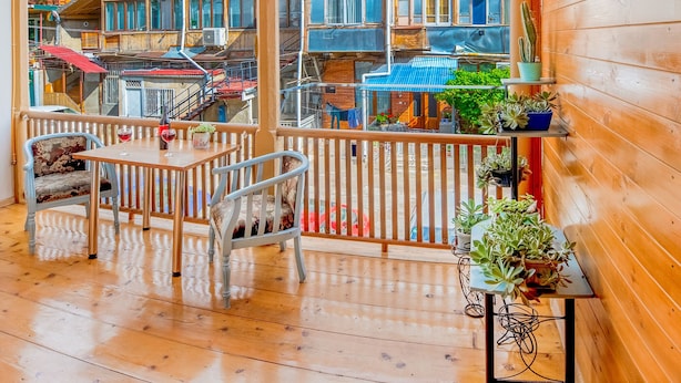 A wooden balcony with a view of adjacent buildings, a table with chairs, and a potted plant. - H&B apartments Qolga (Tbilisi)