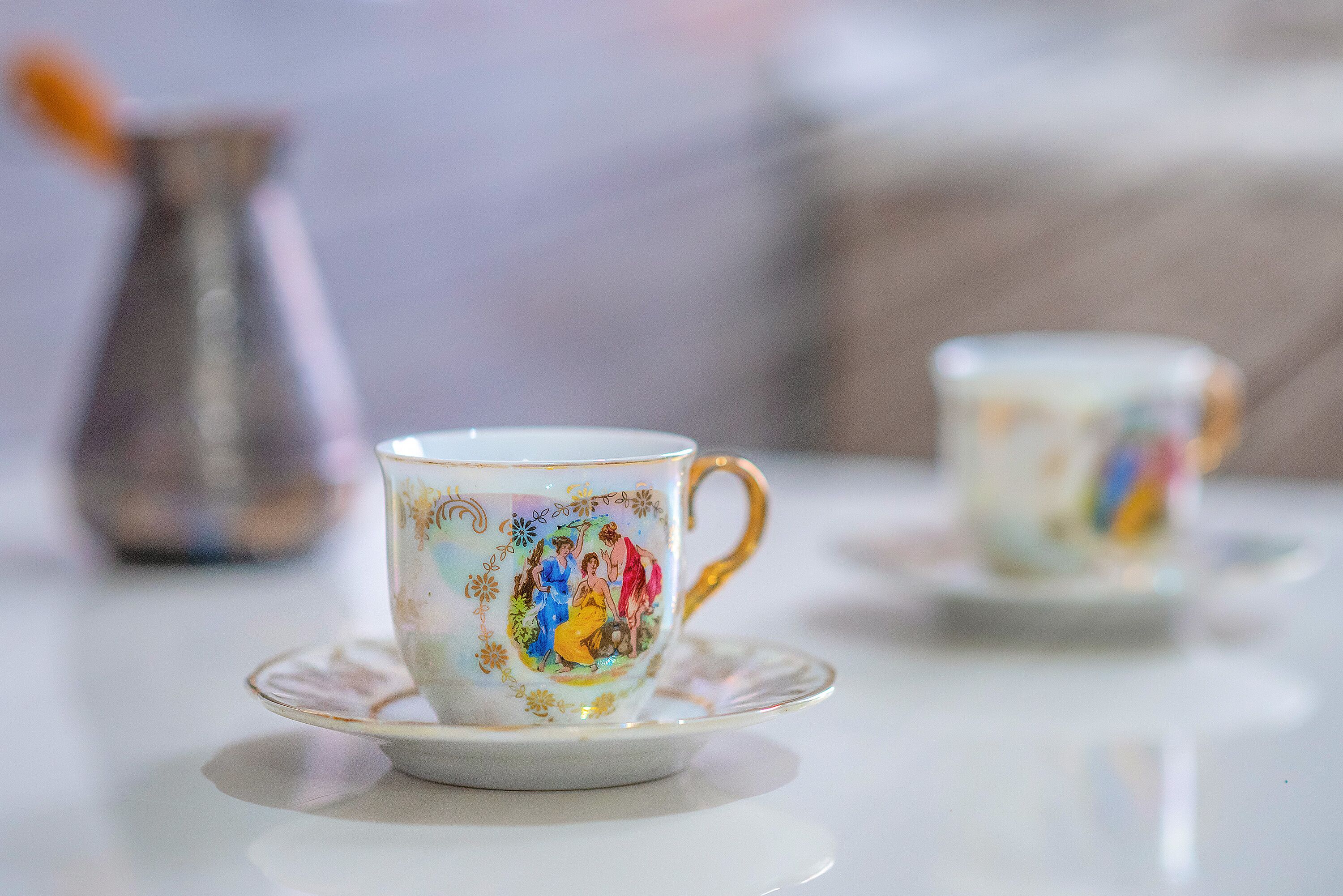 Una mesa blanca con dos tazas y platillos, una con asa dorada y diseño floral.