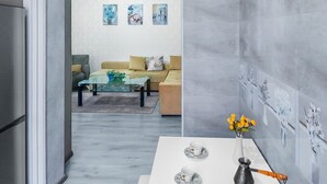 A modern kitchen with a white countertop, a dining table with a vase of flowers, and a view into the living room. - H&B apartments Qolga (Tbilisi)