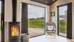 Un interior moderno con una estufa de leña, ventanas amplias y vistas al exterior.