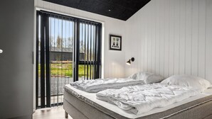 Un dormitorio moderno con una cama grande, vista a través de un ventanal corredero y una lámpara de pared.
